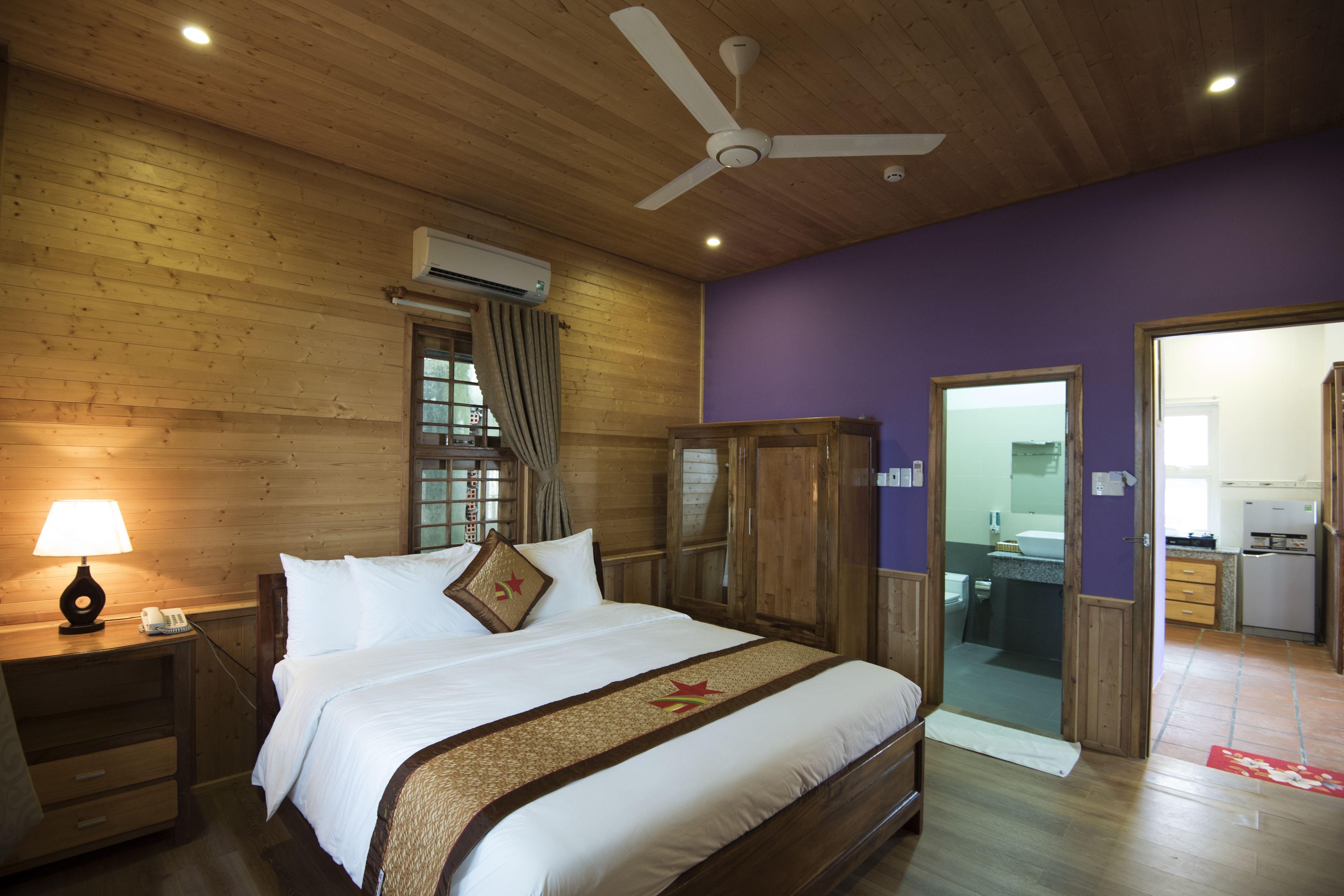 A bedroom with a wooden ceiling, a bed with white bedding, a ceiling fan, and an air conditioning unit.