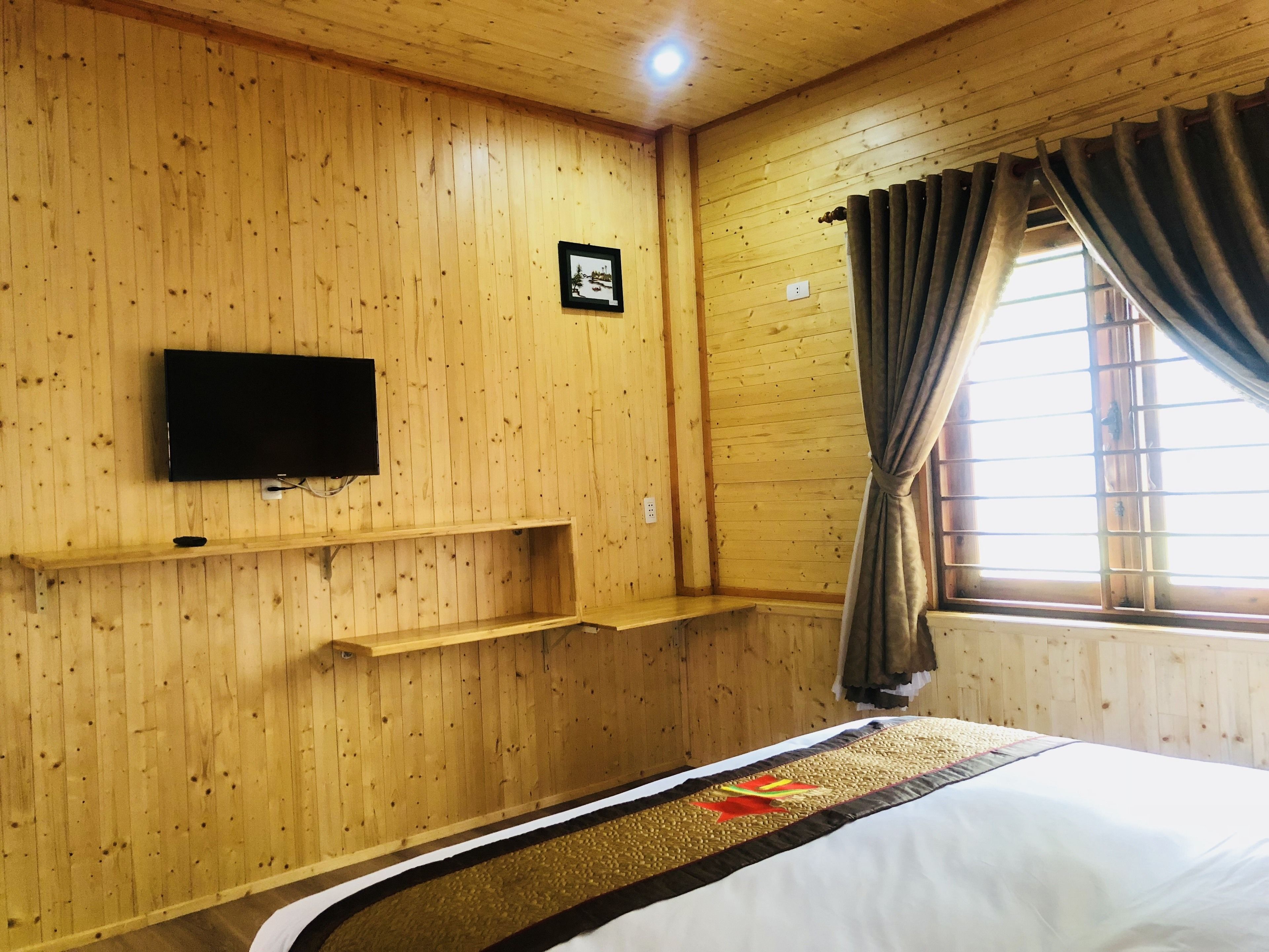 A wooden-paneled room with a bed, a mounted TV, and a window with curtains.