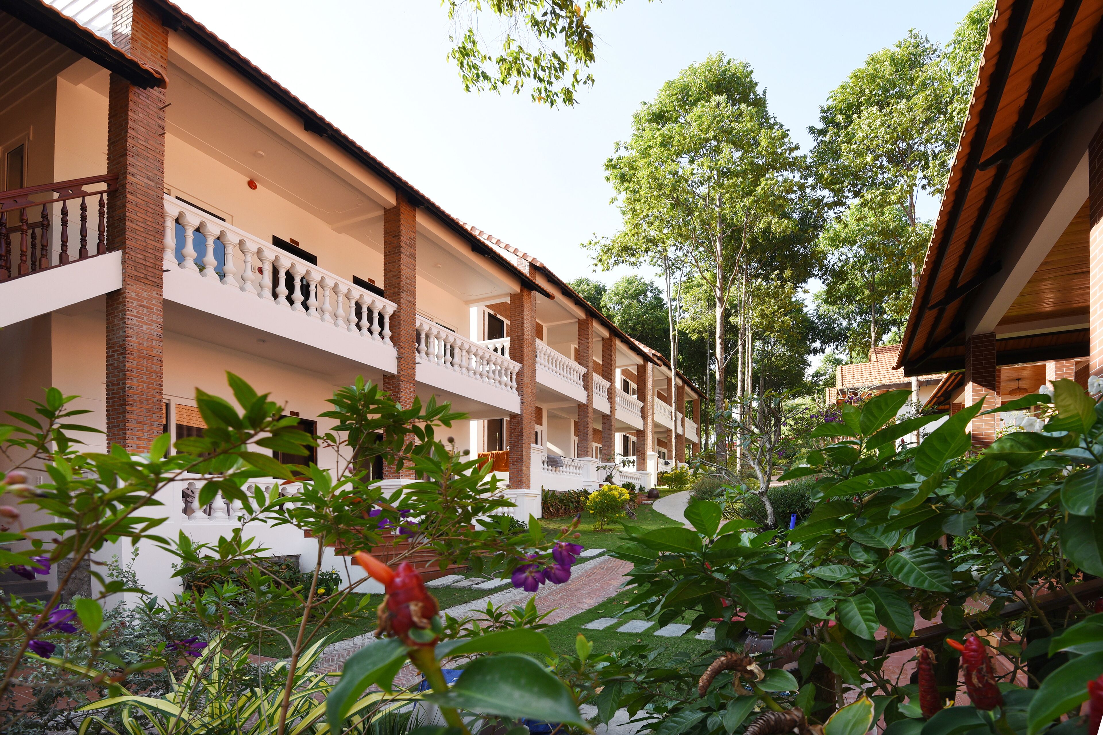 Ein Hotel mit mehreren Balkonen, einer Ziegel-Fassade und einem Gartenbereich mit verschiedenen Pflanzen und Blumen.