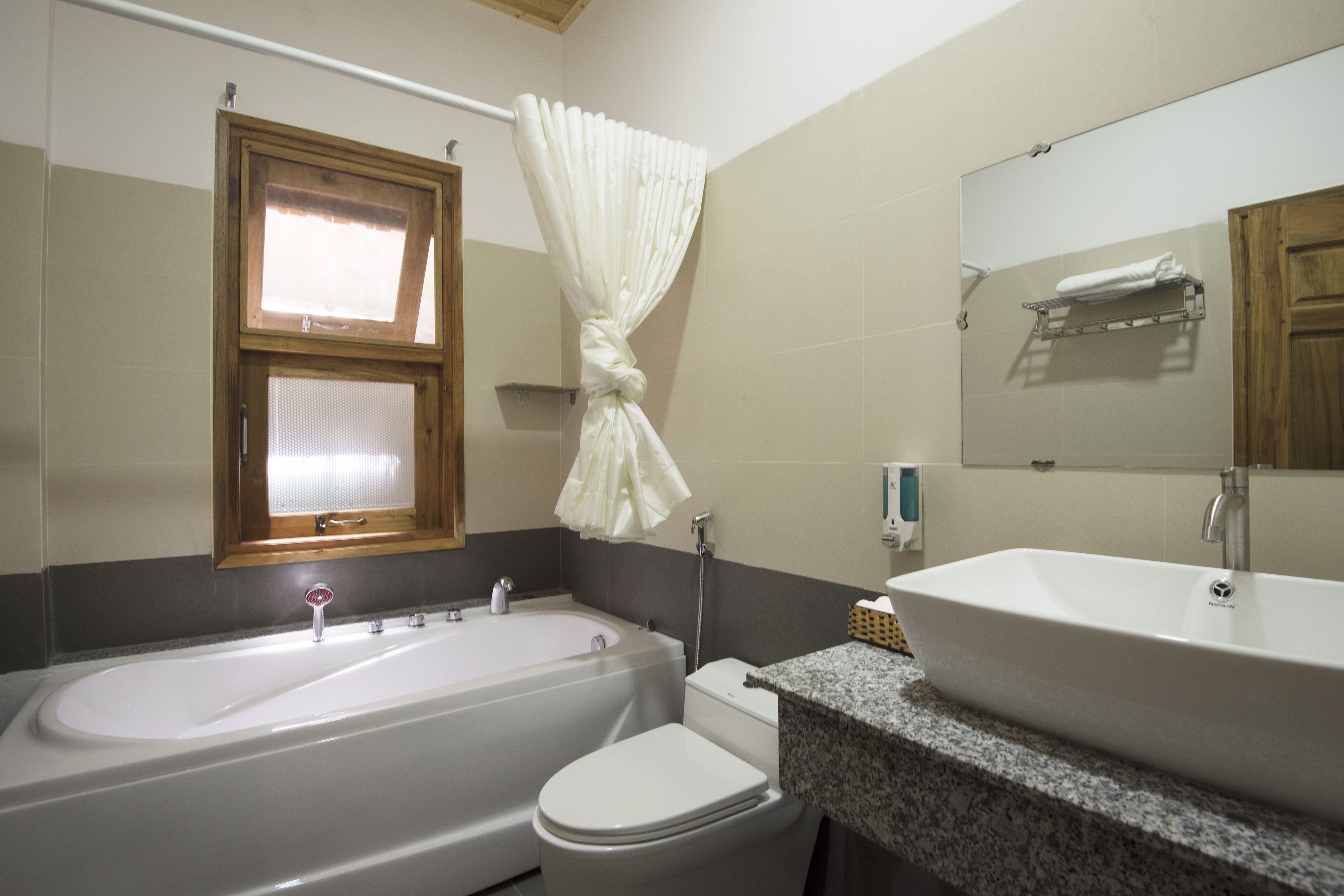 A bathroom with a bathtub, toilet, sink, and a window with a curtain.