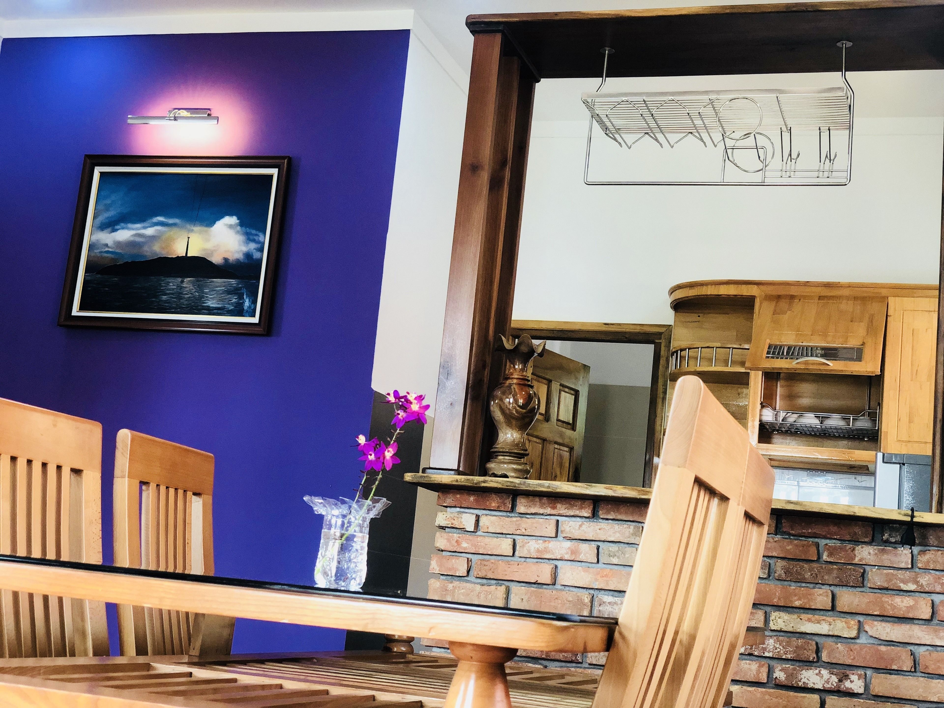 A room with a dining table, chairs, a purple wall, a framed picture, and a brick fireplace.