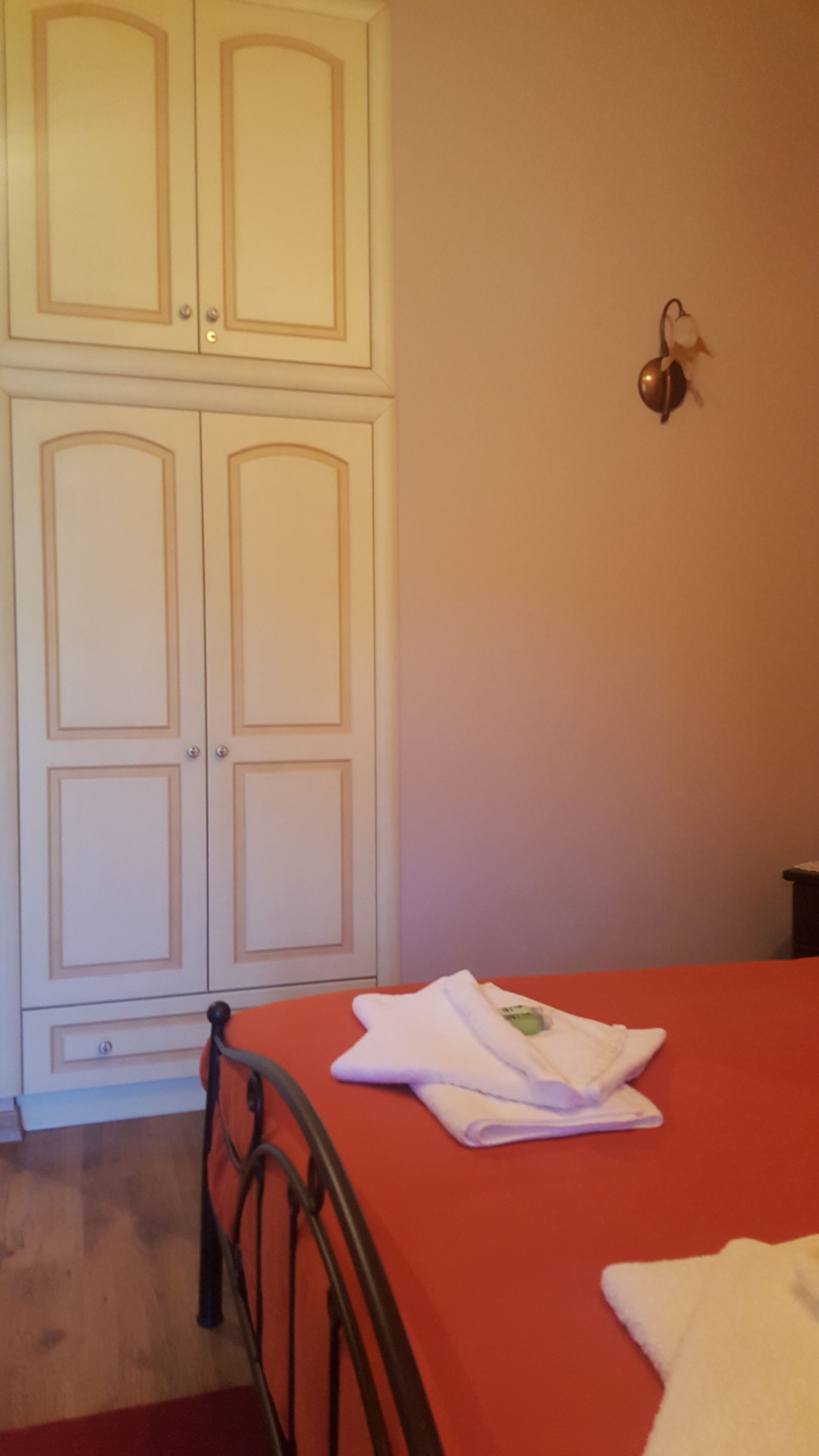 Une chambre avec une couvre-lit rouge, une armoire blanche et un luminaire fixé au mur.