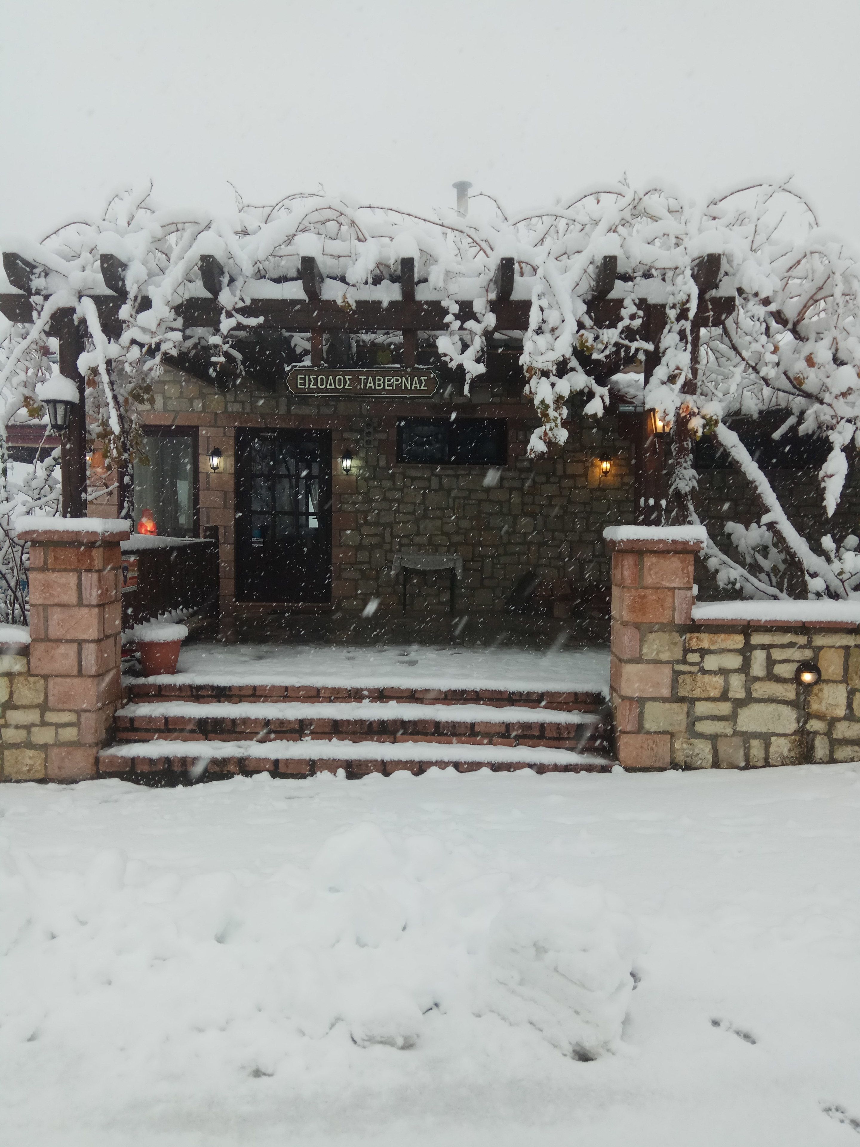 A stone building with a sign reading "EIZODES TABERNAS" and a snow-covered entrance.