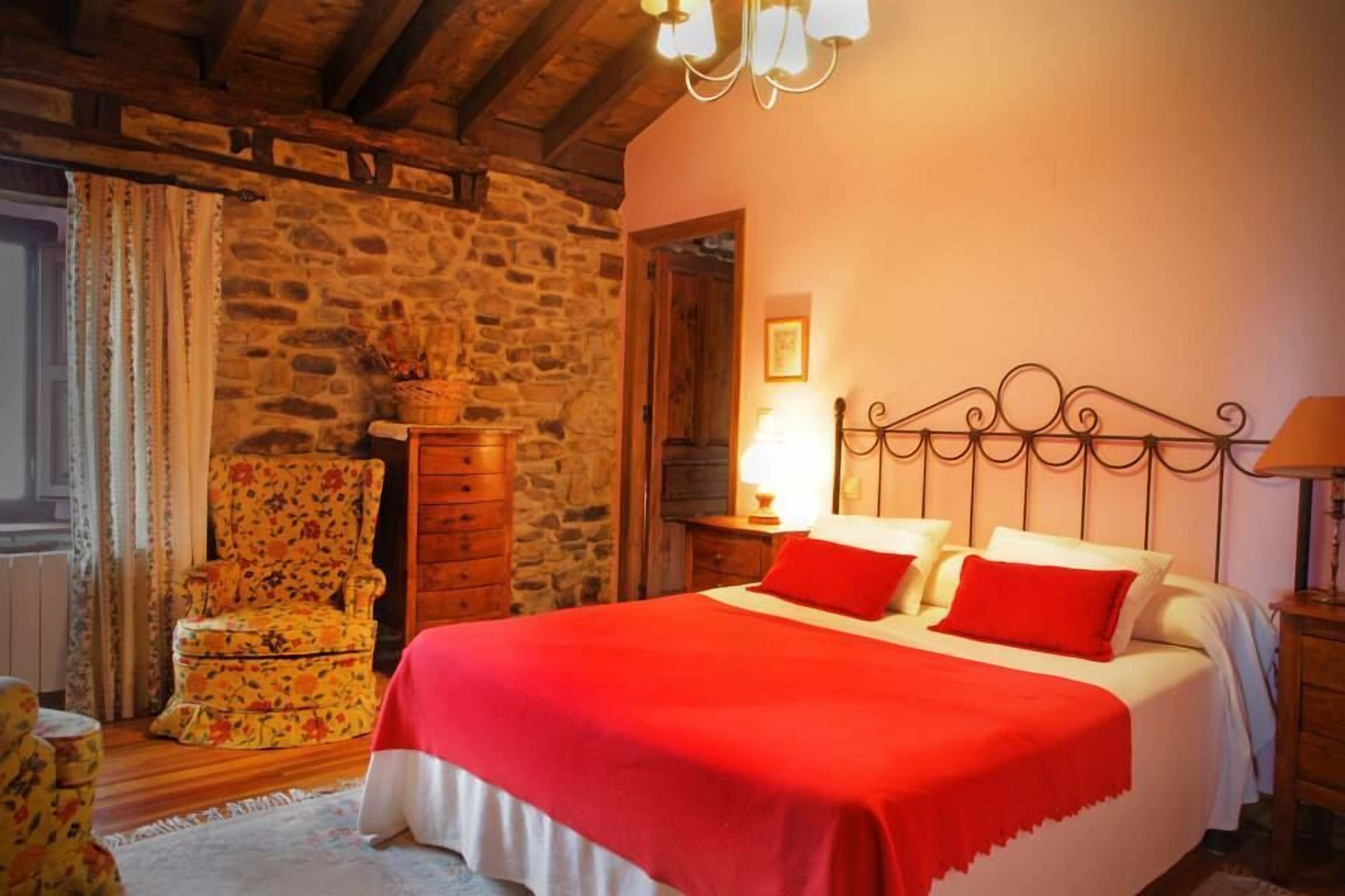 Une chambre confortable avec un mur en pierre, un cadre de lit en bois et un fauteuil à motifs floraux.