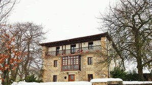 A stone building with a balcony, surrounded by snow and trees. - El Cajigal De Quintana (Espinosa de los Monteros)