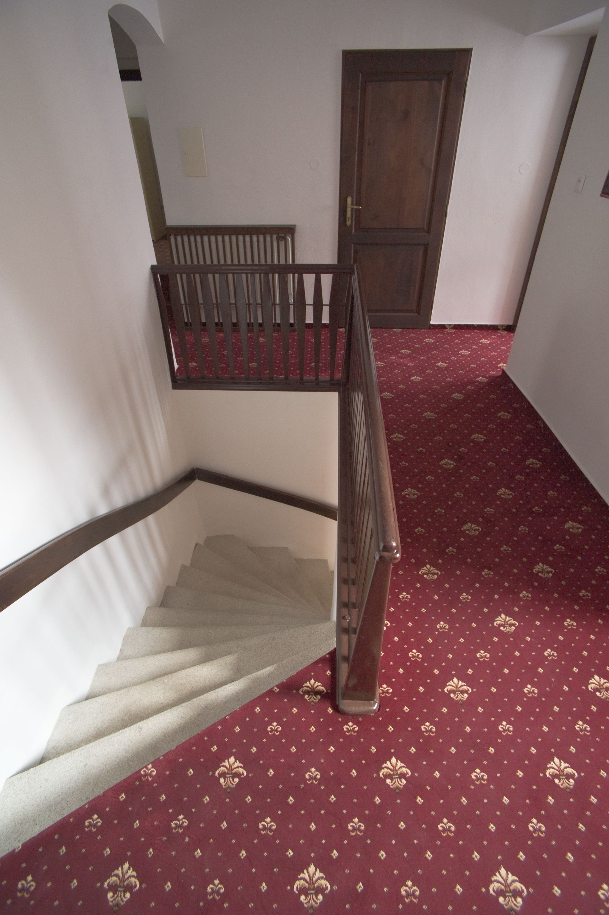 A staircase with a wooden handrail and a red patterned carpet.