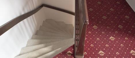 A staircase with a wooden handrail and a red patterned carpet.