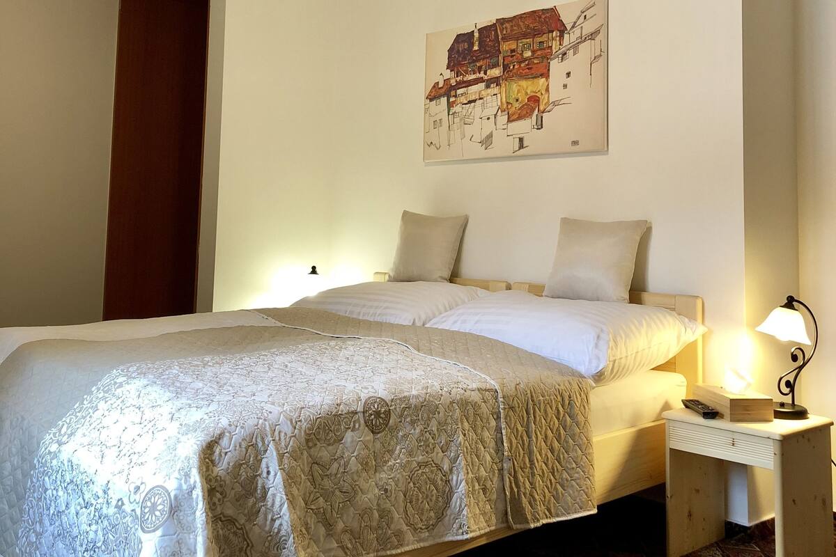 Ein Schlafzimmer mit einem Bett, Nachttischen, einem Wandbild und einer Deckenleuchte.