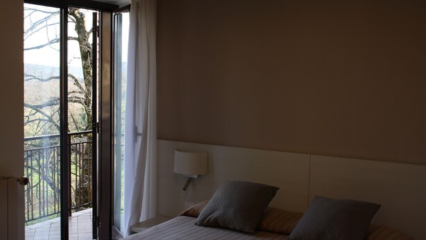 A bedroom with a bed, a nightstand with a lamp, and a view of a balcony with a railing. - Krizman (Monrupino)