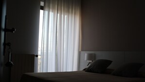 A dimly lit hotel room with a large bed, a bedside lamp, and sheer curtains allowing natural light. - Krizman (Monrupino)