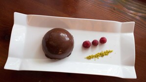 A white plate with a chocolate-covered item and raspberries on a wooden table. - Krizman (Monrupino)