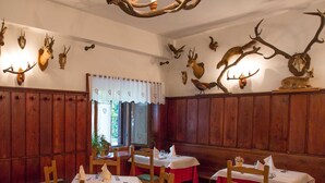 A restaurant with wooden paneling, tables with red tablecloths, and antler decorations on the walls. - Krizman (Monrupino)