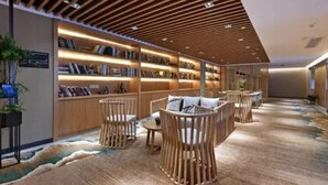 A modern library with wooden bookshelves, comfortable seating, and a patterned carpet. - Mehood Lestie Hotel Panyu Branch (Guangzhou)