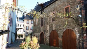 A narrow cobblestone street with stone buildings, wooden doors, and a small garden with flowers.