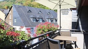A terrace with a table and chairs, overlooking a building with a sloped roof and a water tower in the background.
