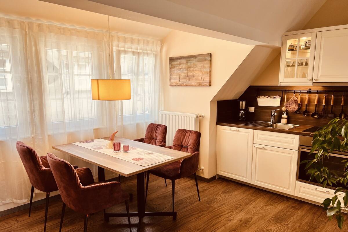 Ein Essbereich mit Tisch, Stühlen und einer Lampe. Es gibt eine Küche mit Schränken und einer Arbeitsfläche.