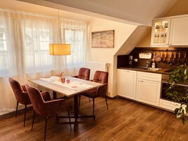 Un comedor con mesa, sillas y una lámpara. Hay una cocina con armarios y una encimera.