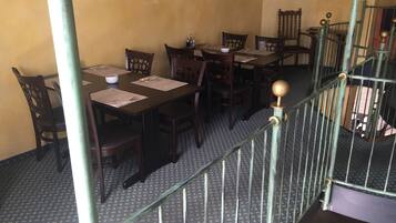 Un espace repas avec des tables et des chaises en bois, un escalier doté d’une rampe en métal et des carreaux de sol à motifs.