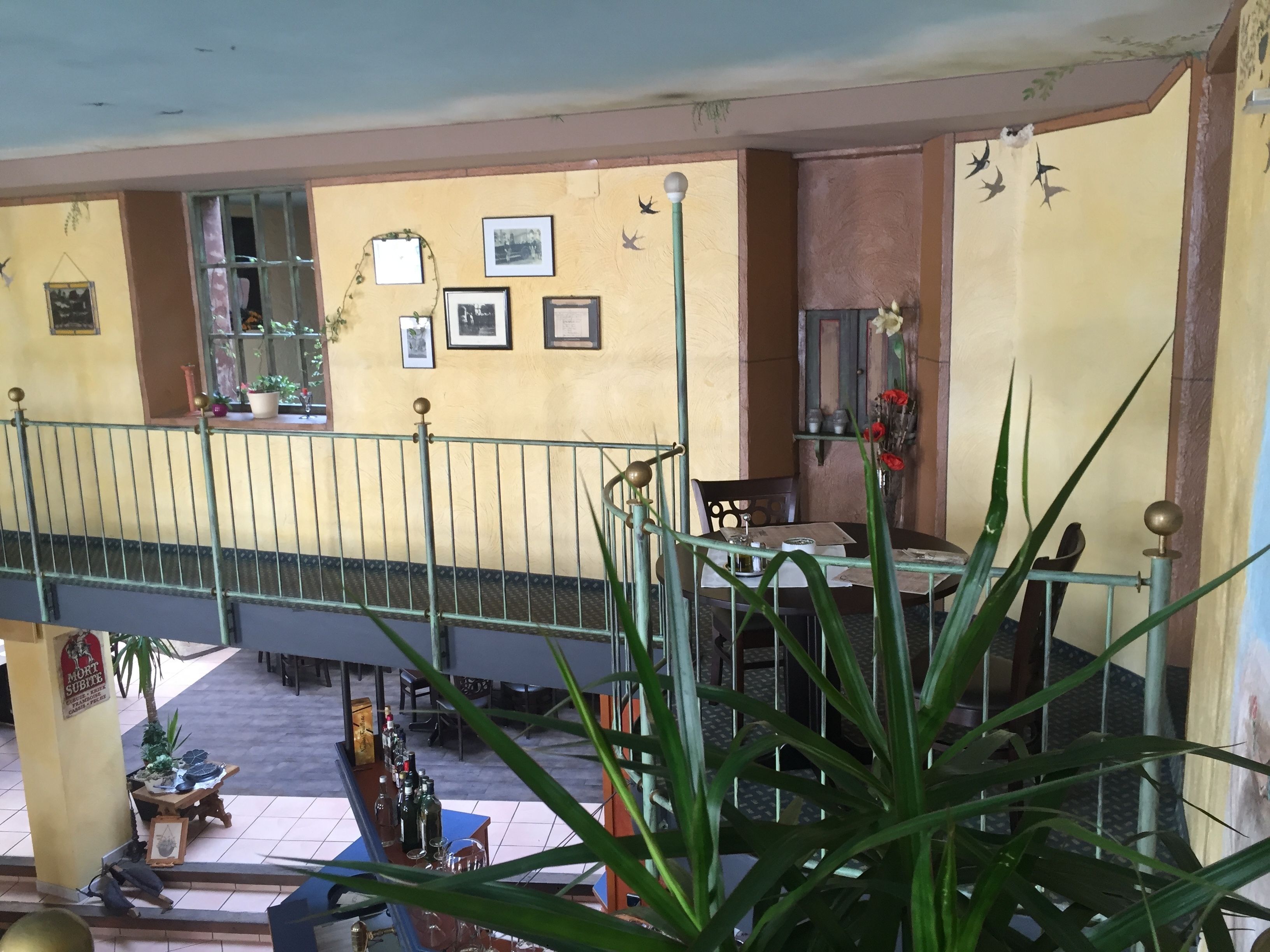 Un balcone con ringhiera in metallo, un tavolo con sedie e vista sulla strada sottostante.