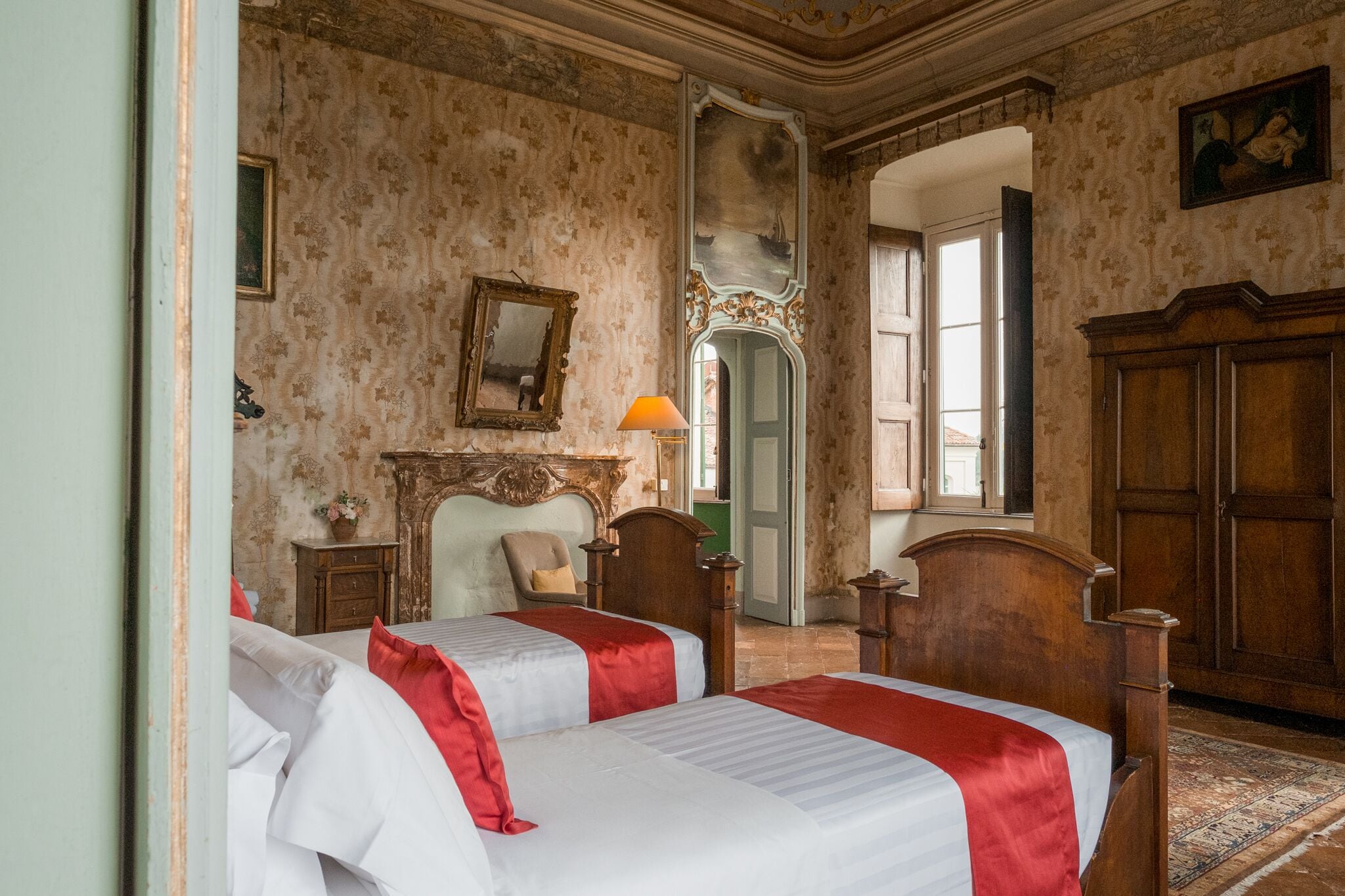 Une chambre avec deux lits, une armoire en bois, un miroir et une porte donnant sur une autre pièce.