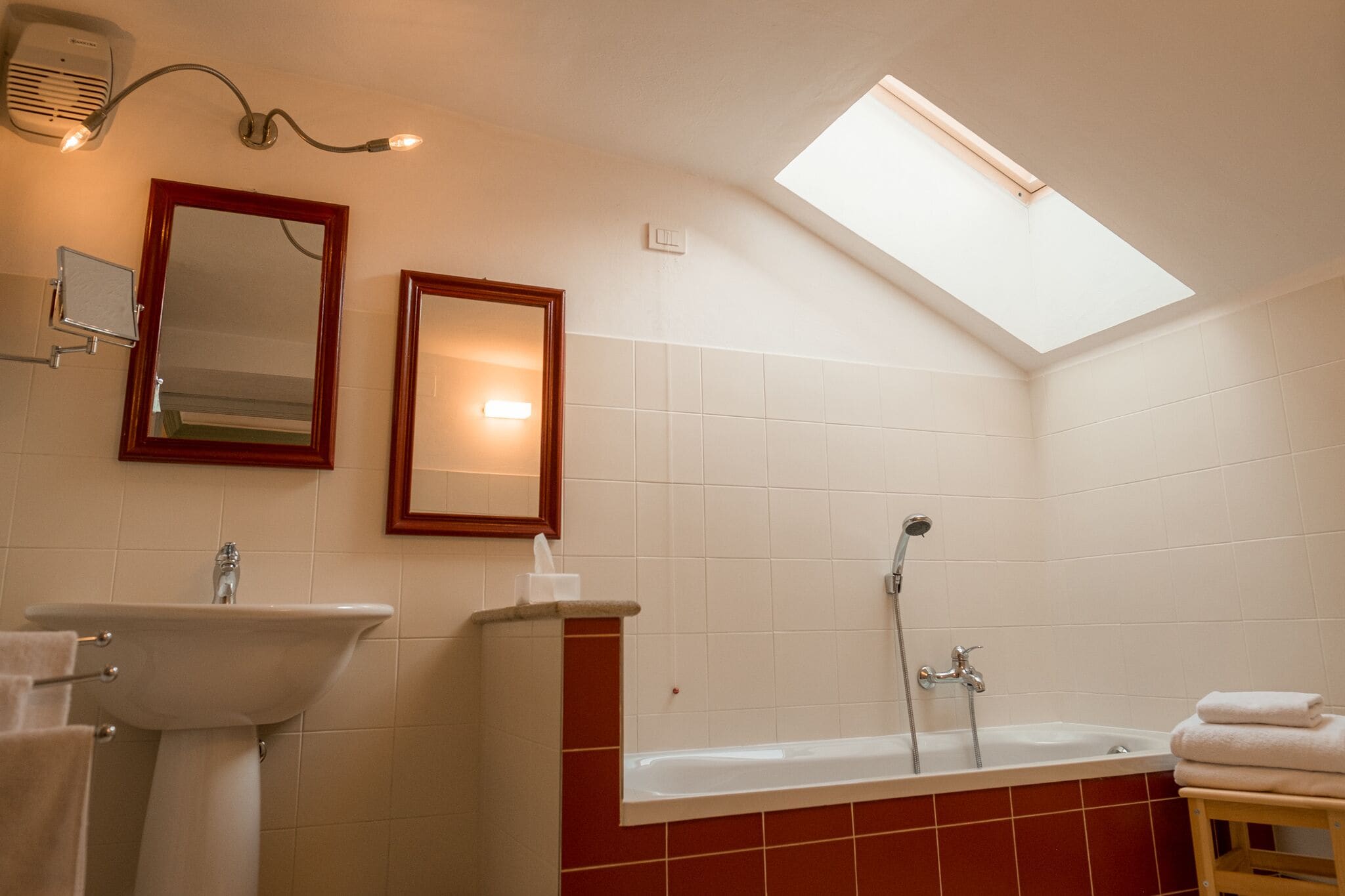 Un baño con tragaluz, lavamanos, espejo y bañera.