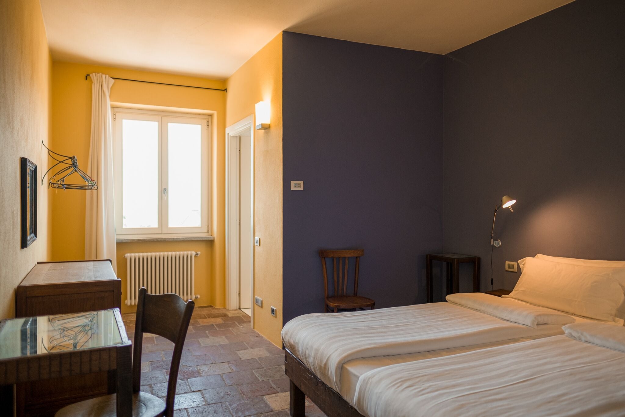 A bedroom with a bed, a chair, a table, and a window with curtains.