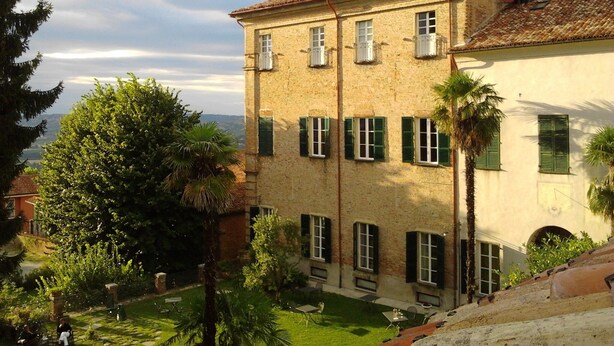 A two-story building with a courtyard, featuring a brick facade, green shutters, and multiple windows. - Albergo Real Castello (Verduno)