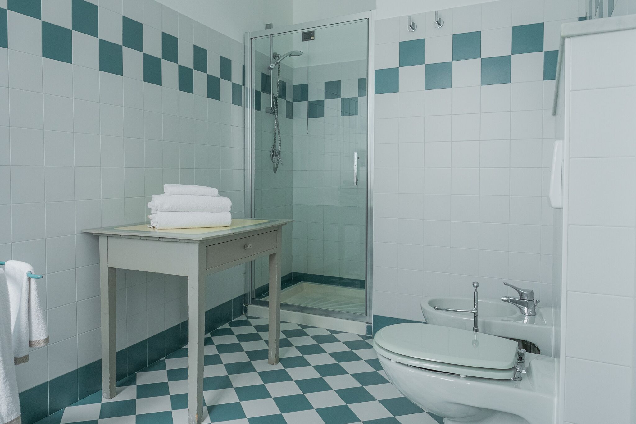 Een badkamer met een zwart-wit geruite vloer, een douche met glazen wand, een wastafel en een toilet.