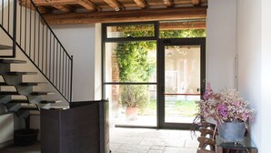 A spacious interior with a wooden ceiling, a staircase, and a large glass door leading outside. - Albergo Real Castello (Verduno)