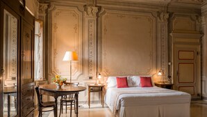 A hotel room with a large bed, a wooden desk, a lamp, and ornate wall decorations. - Albergo Real Castello (Verduno)