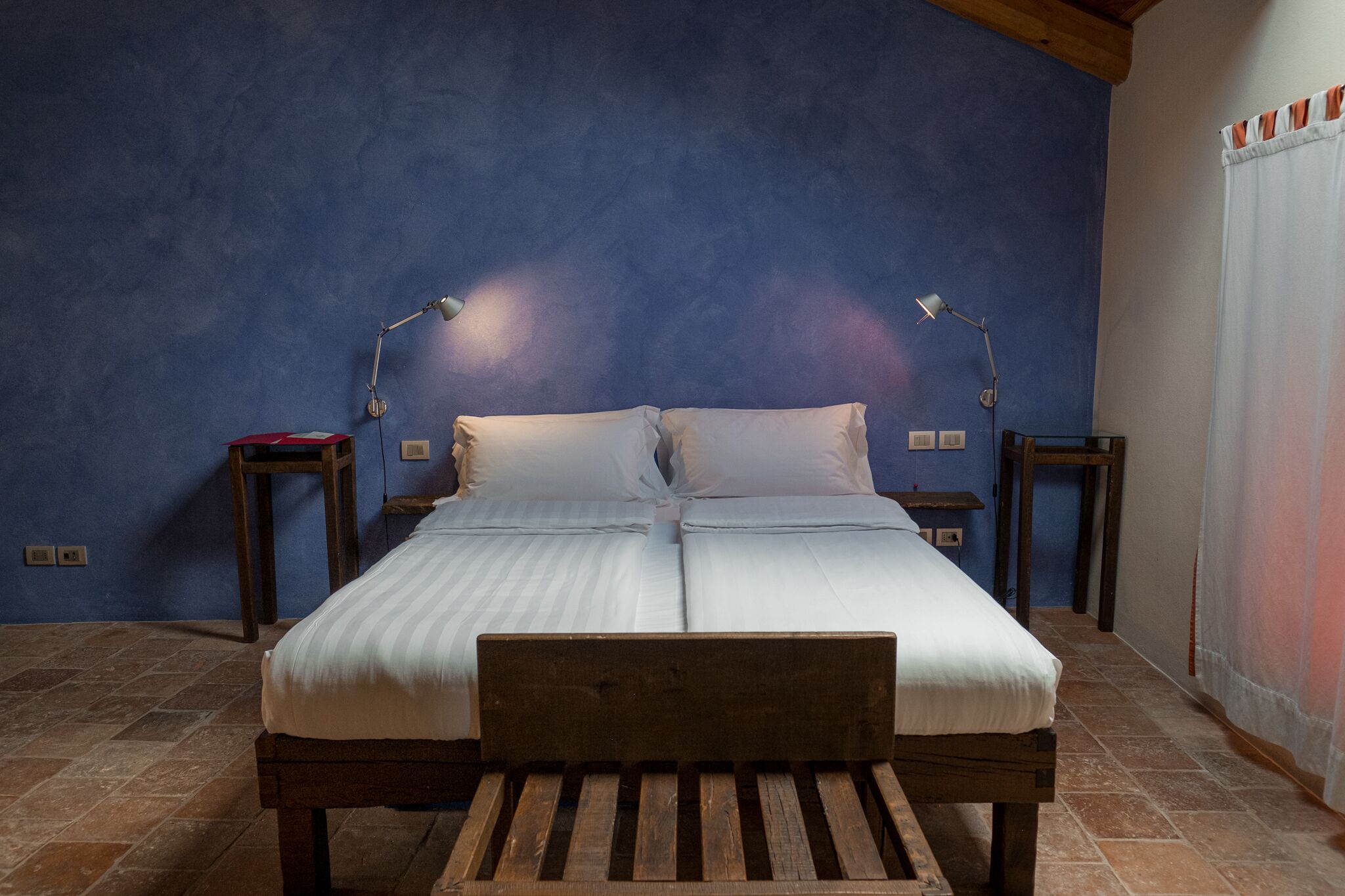 A double bed with a wooden headboard, two bedside tables with lamps, and a blue textured wall.