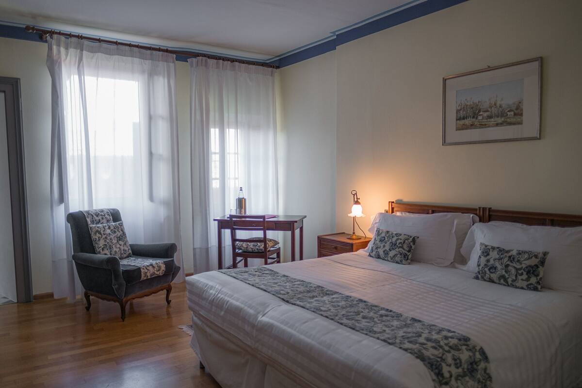 A bedroom with a large bed, a chair, a desk, and a nightstand.