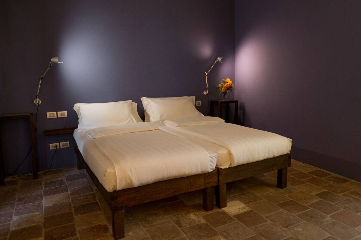 A neatly made bed in a room with purple walls and a tiled floor.