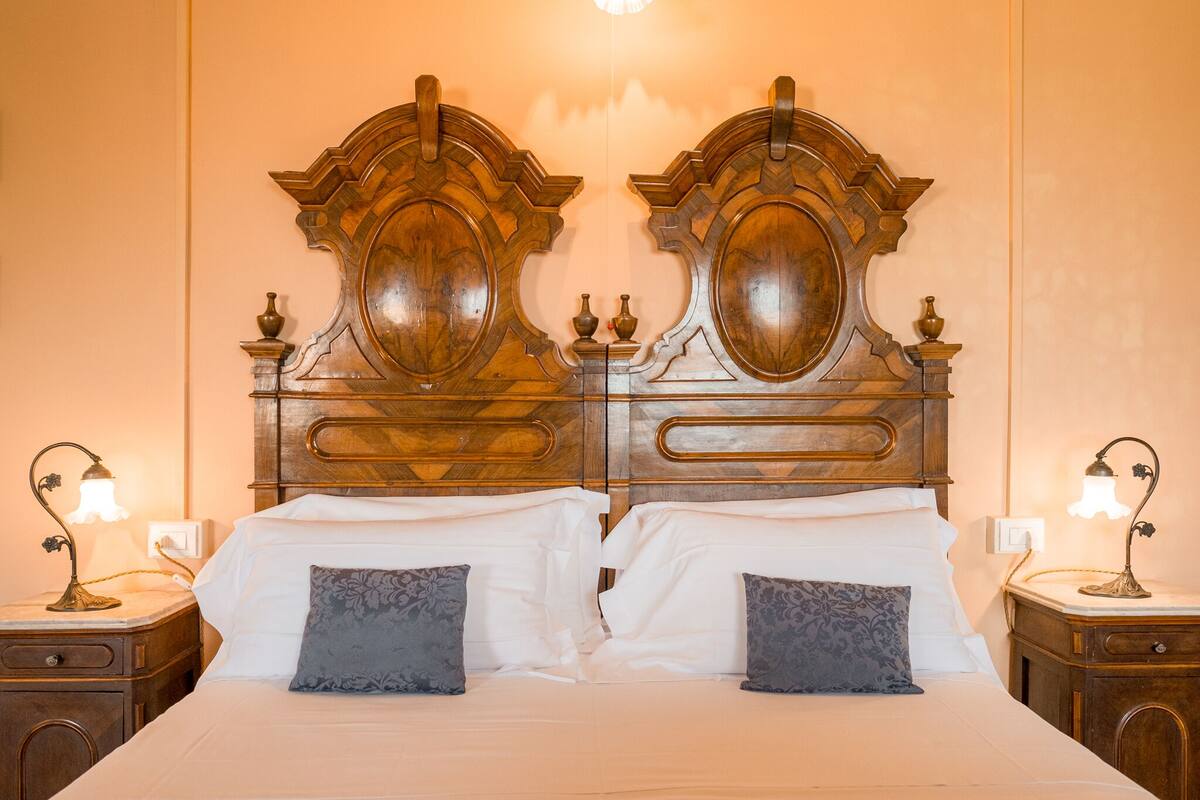 A double bed with a wooden headboard, two bedside tables with lamps, and a nightstand with a lamp.