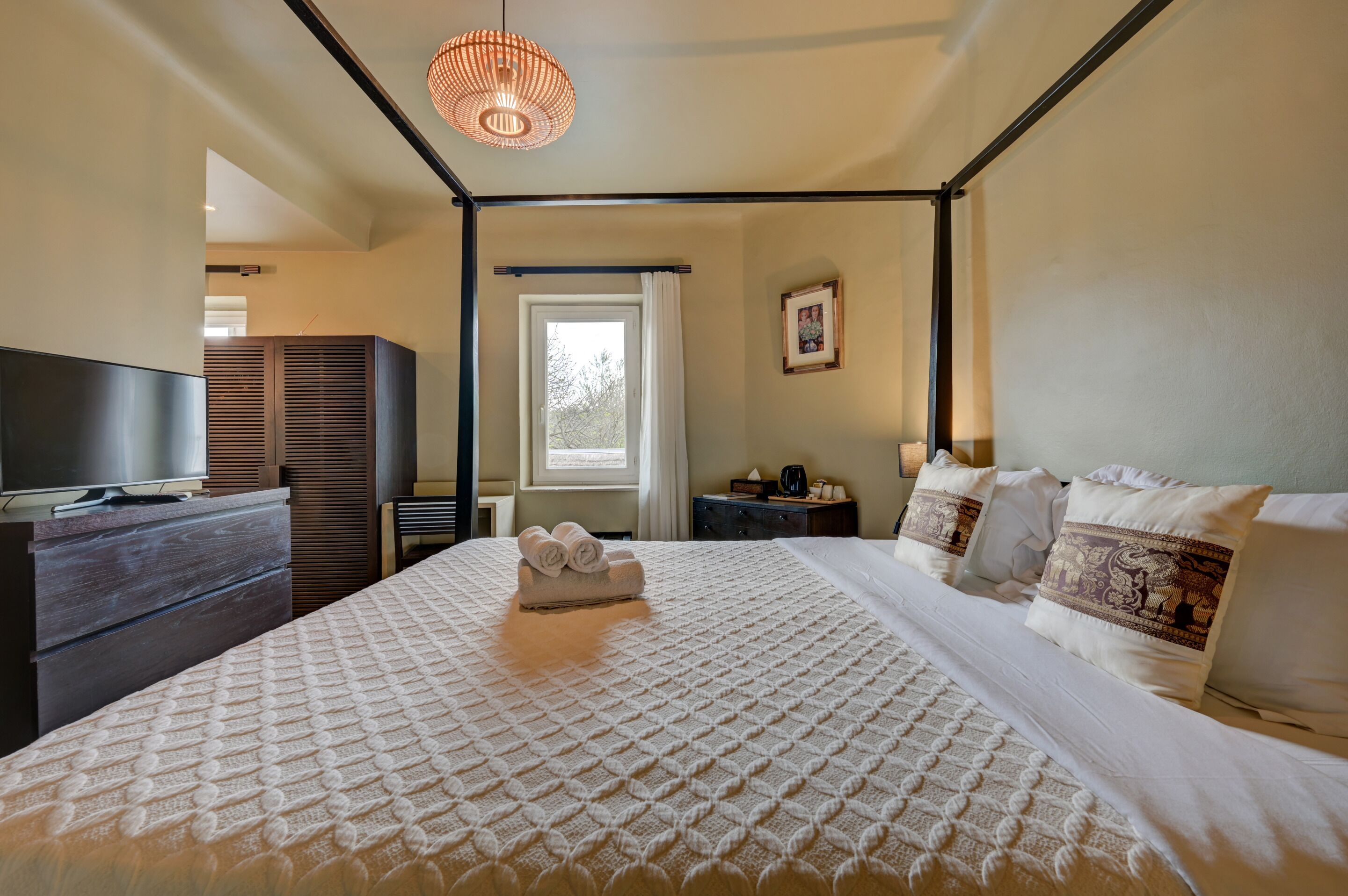 A bedroom with a four-poster bed, a television, a dresser, and a window with curtains.