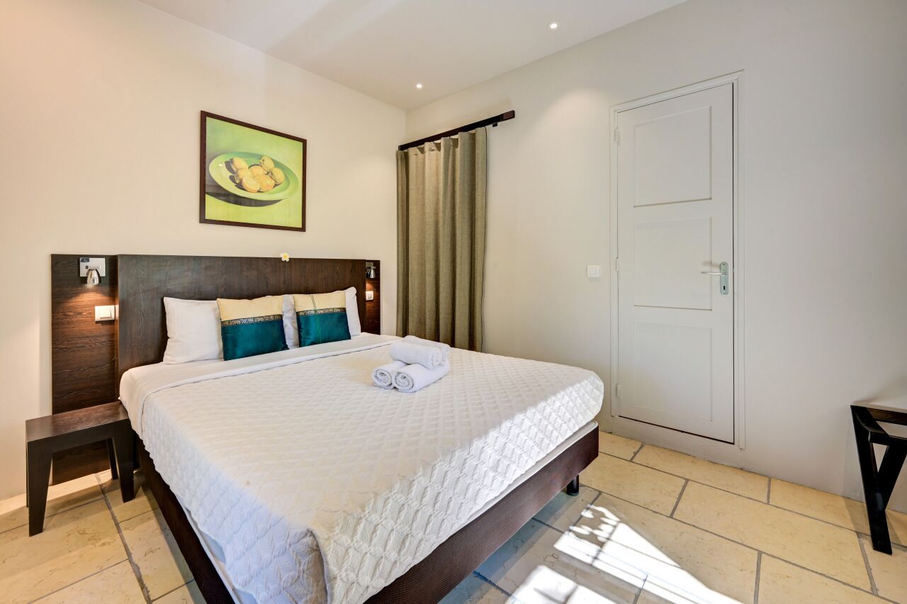 Une chambre d’hôtel avec un grand lit, une tête de lit dotée d’un luminaire, une porte et un tableau au mur.