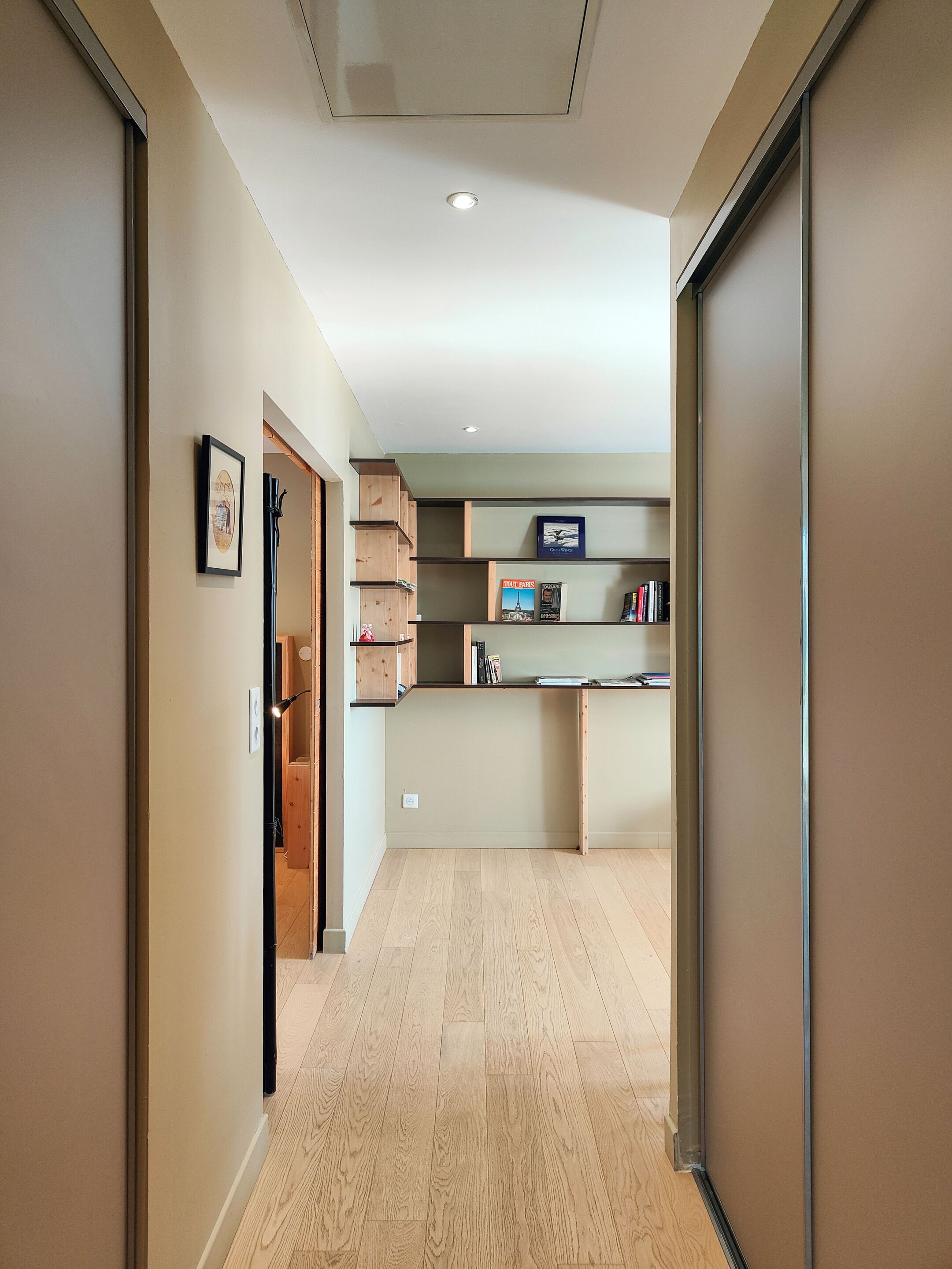 A hallway with a wooden floor, a kitchen area with a built-in shelf, and a framed picture on the wall.