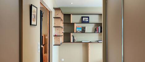 A hallway with a wooden floor, a kitchen area with a built-in shelf, and a framed picture on the wall.