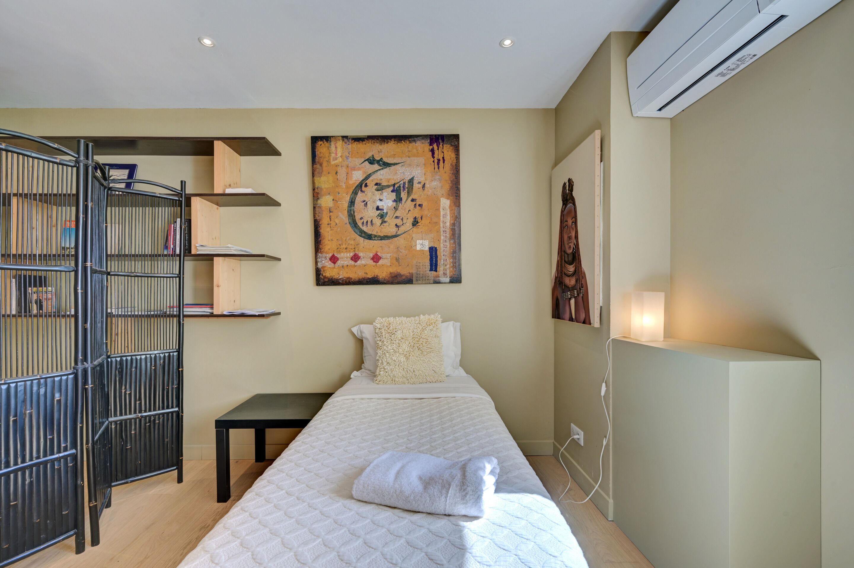 A hotel room with a bed, a black metal gate, a wall-mounted shelf, and a large abstract painting.