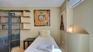 A hotel room with a bed, a black metal gate, a wall-mounted shelf, and a large abstract painting.