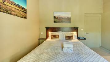 A hotel room with a bed, a headboard, a nightstand, a door, and two wall-mounted pictures.