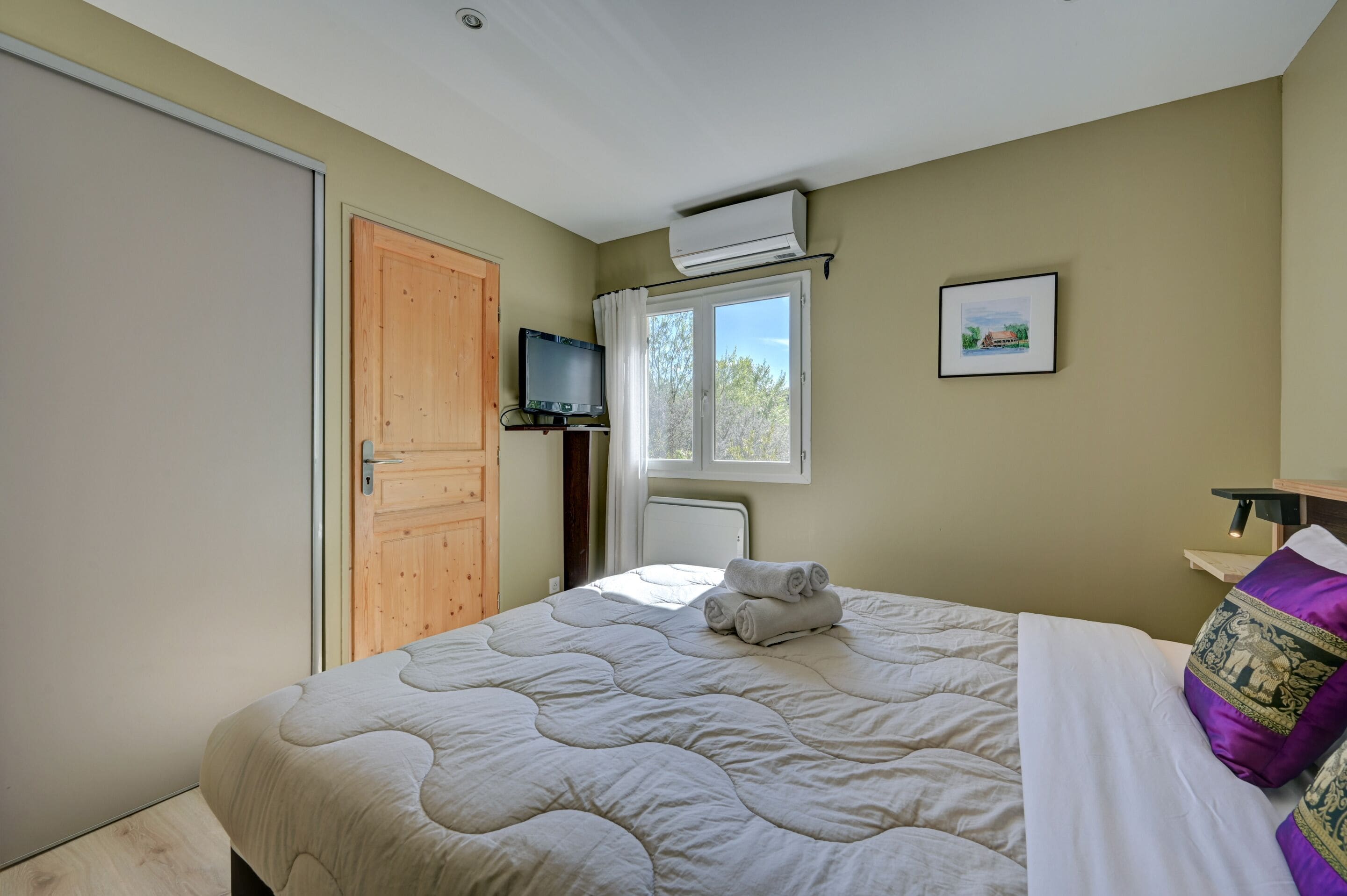 A bedroom with a bed, a TV, an air conditioner, a window, and a door.