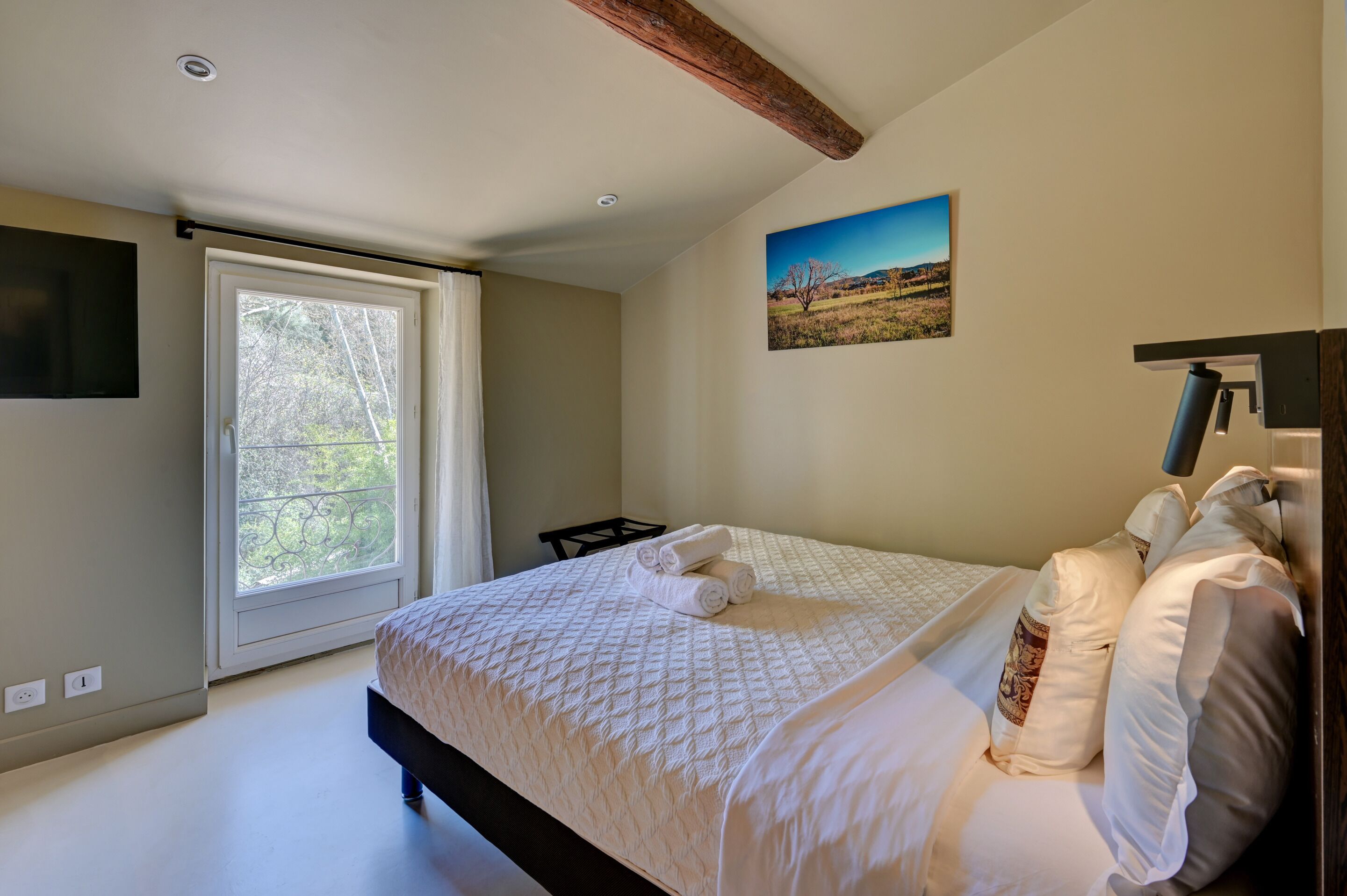 A bedroom with a large bed, a window with a view of greenery, and a painting on the wall.