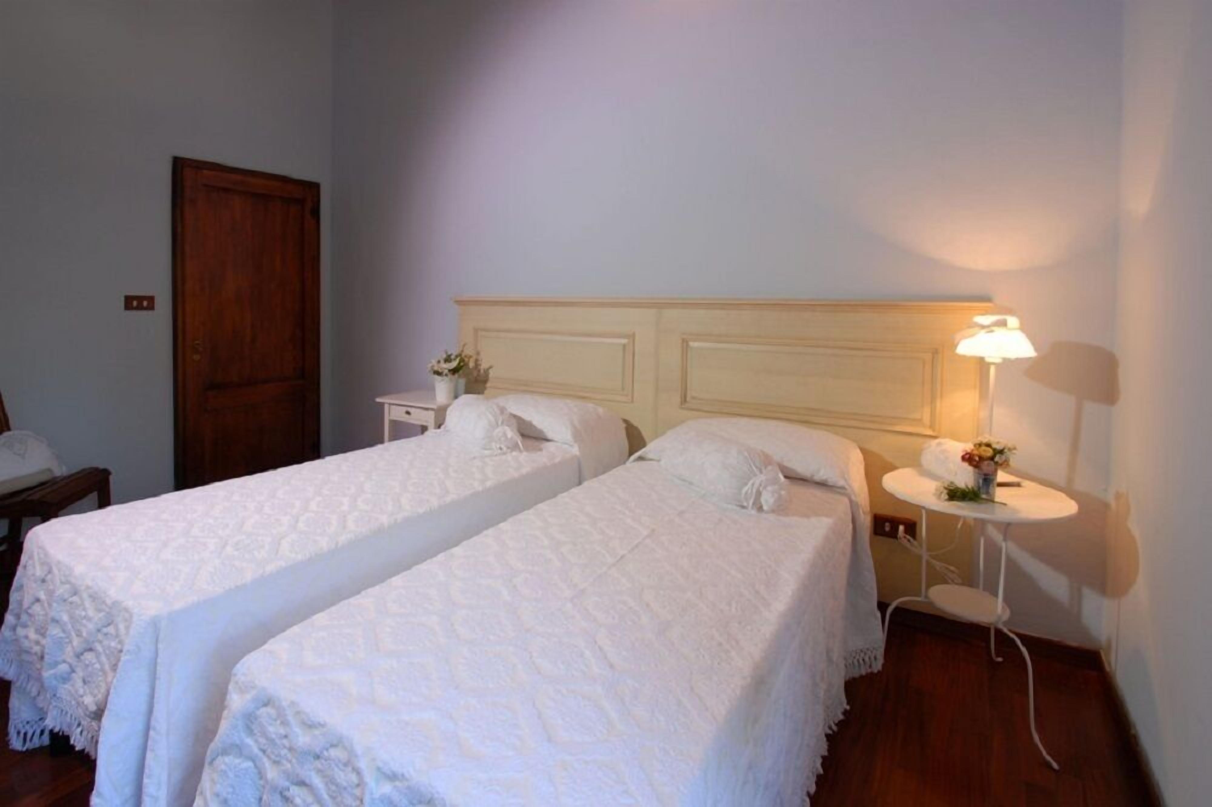 Une chambre avec deux lits simples, une porte en bois, une petite table de chevet avec une lampe et un téléphone fixé au mur.