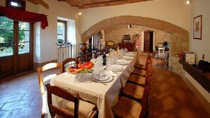 A dining area with a long table set for a meal, stone arches, and a view of the outdoors.