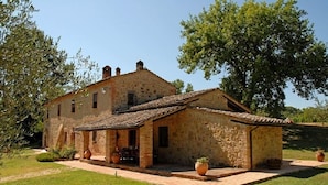 A rustic stone building with a tiled roof, a covered patio area, and potted plants.
