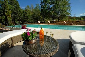 Un espace aménagé au bord de la piscine, avec une table en osier, des chaises longues et un pot de fleurs.
