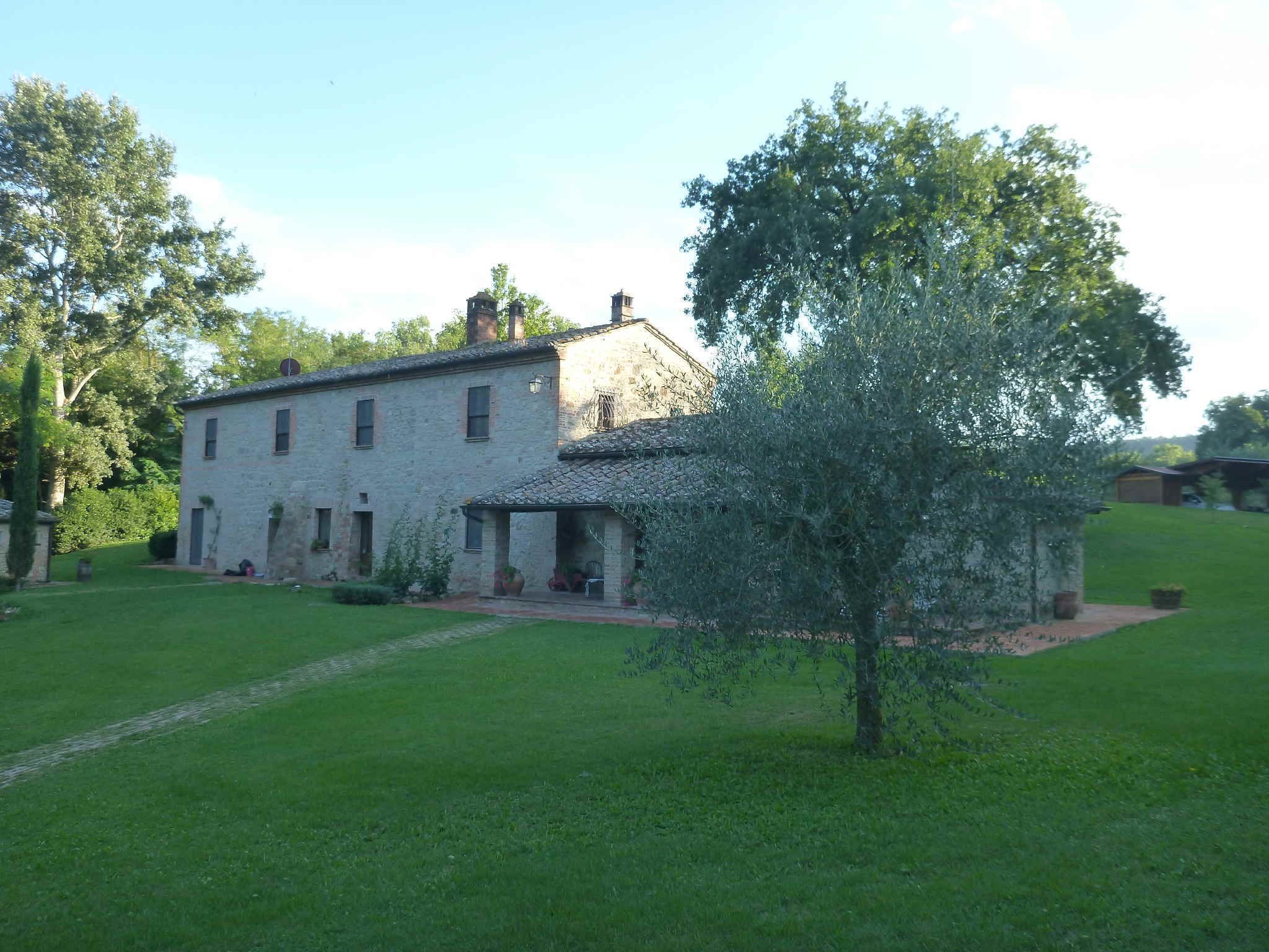 A stone building with a tiled roof, surrounded by a well-maintained lawn and trees.