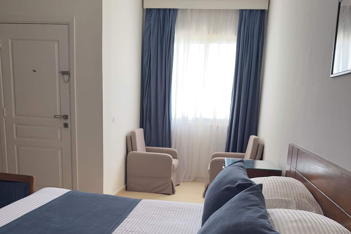 A hotel room with a bed, a chair, a small table, and a window with curtains.