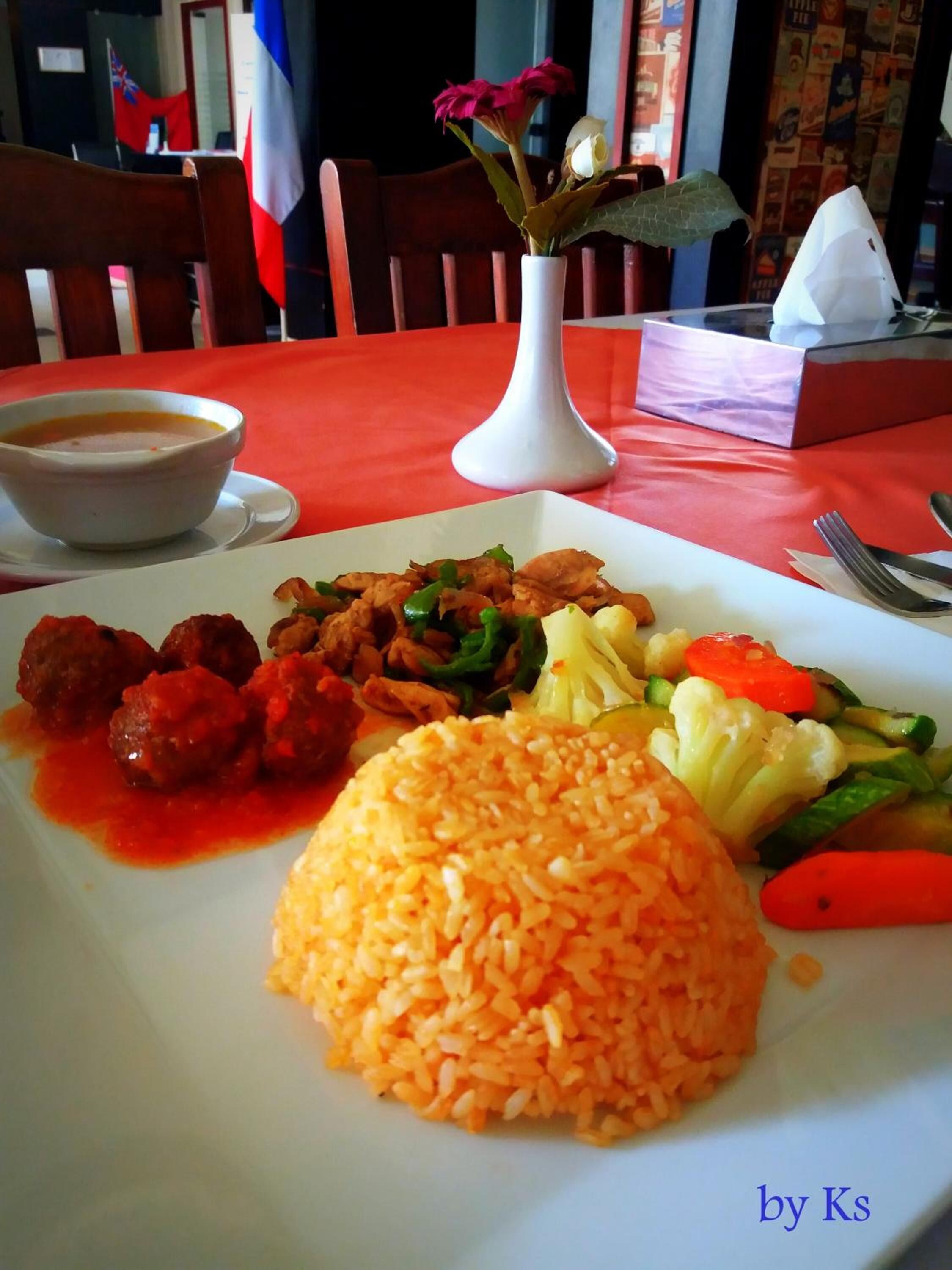 A plate of food with rice, meatballs, vegetables, and a bowl of soup.